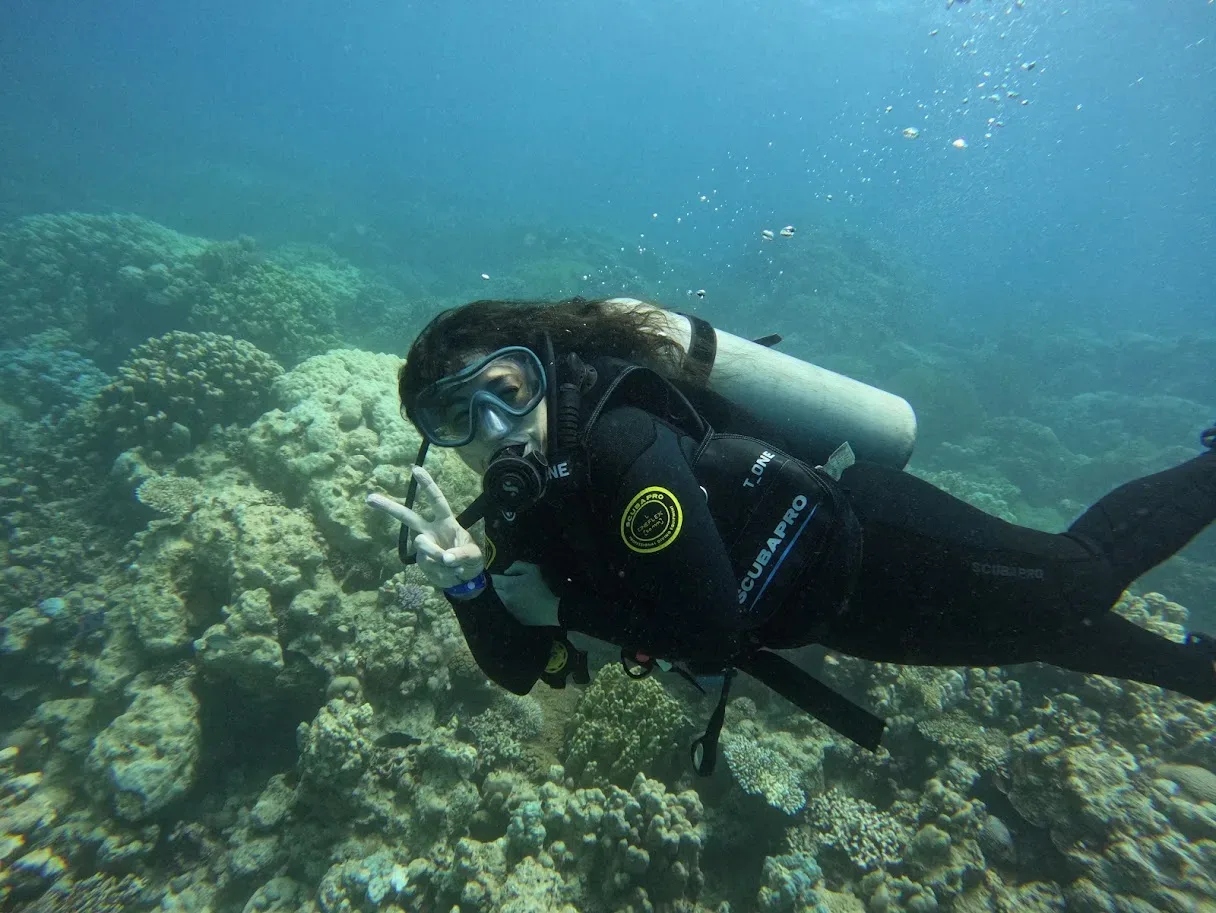 Sarah in immersione tra i coralli, con maschera e bombole, che fa il segno della vittoria